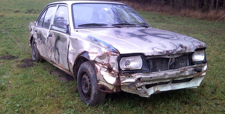 En sprayad grå skrotbil ute på ett fält