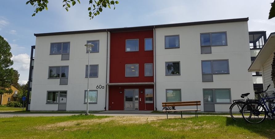 3 våningar vitt hyreshus, inglasade balkonger, solig dag