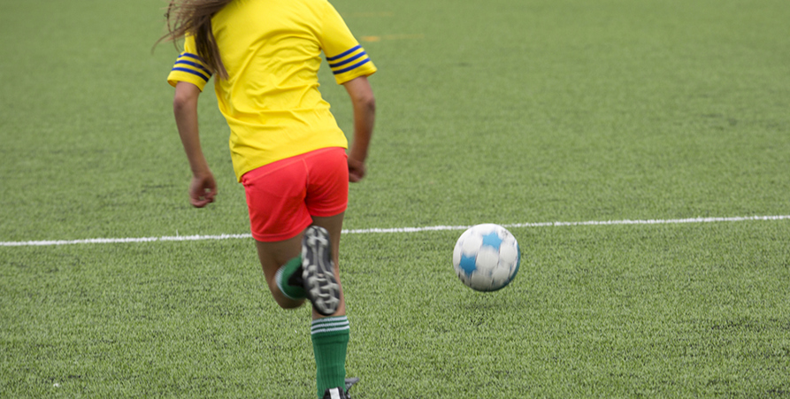 Ung tjej som springer med boll på fotbollsplanen. 